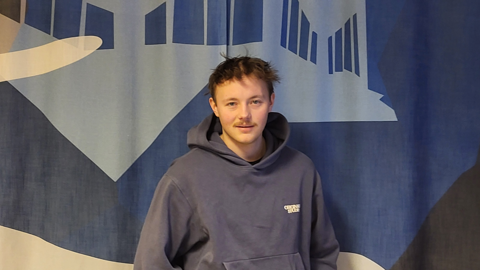 Gabriel, studerande på utbildningen Processtekniker med vätgaskompetens, står framför en blå vägg med grafiskt mönster och bär en blå hoodie.